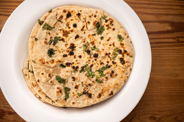 Close-up of traditional Indian chapatti (roti) garnished with coriander leafs served in white plate.