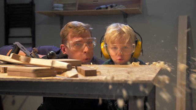Boy and man blow off wooden shavings from the table, slow motion