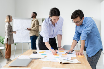 Fototapeta premium Young multi-ethnic colleagues standing at desk and planning project strategy in office