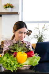 Beautiful woman smiling search how to cooking salad from internet by computer in kitchen.