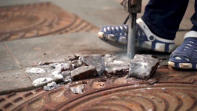 A jackhammer worker smashes a marble slab around an iron hatch