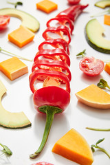 Selective focus of microgreens, cut chili pepper, pumpkin and cherry tomato with avocado slices on white