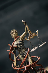 Scales of Justice, Justitia, Lady Justice and barbed wire on a black wooden background.