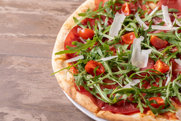 close up of delicious italian fresh pizza with ham, arugula, tomato and parmesan