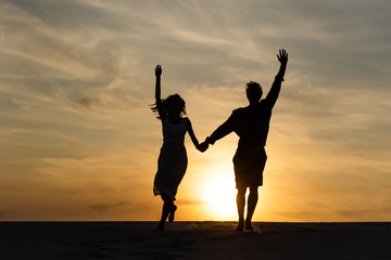 Plakat silhouettes of man and woman running on beach against sun during sunset