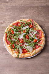 close up of delicious italian fresh pizza with ham, arugula, tomato and parmesan