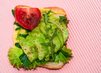 Pink background and square toast with avocado, cherry tomato, arugula and salad. Useful and delicious breakfast.