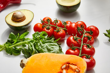 Selective focus of pumpkin, cherry tomatoes, basil and avocado halves on white background