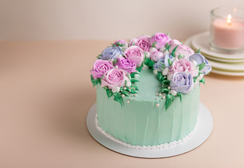 A turquoise cake with cream roses for a wedding. On a pink background. With a pink candle on white plates