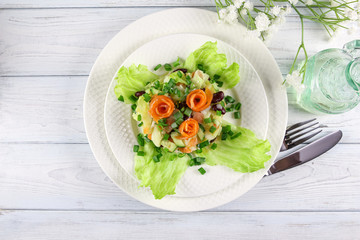 Salmon salad with fresh cucumber, red beans on lettuce leaves, served on a white porcelain plate. On a light wooden background with cutlery and olive oil in a glass bottle. Top view