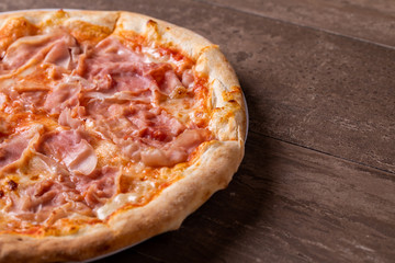 details of pizza with mozzarella and ham on a wooden background
