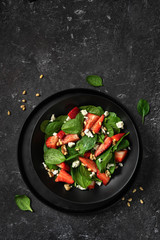 Vertical shot of fresh strawberry spinach salad with feta cheese and nuts on black background