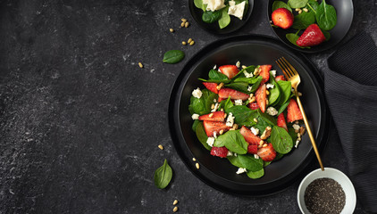 Top view of a black plate of strawberry spinach salad and its ingredients