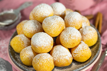 Small homemade curd donuts with icing sugar on a gray concrete background with a pink napkin. Close-up