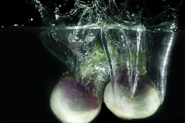 Turnips dropping down in water with water bubbles and splashes under water Turnips food photograph on black background