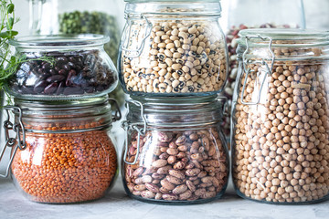 Set of different legumes in glass jars on, concrete white table. A source of protein for vegetarians. The concept of healthy eating and food storage.