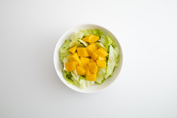 lettuce salad and mango in a white bowl.