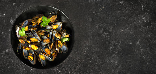 Top view of freshly cooked mussels in a black plate on dark background