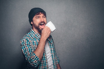 Handsome bearded man in casual clothes with coffee cup laughing with beanie on isolated background