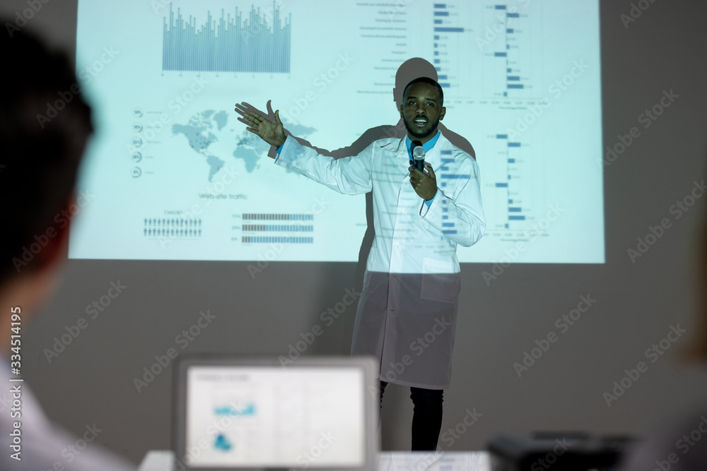 Poster confident young afro-american medical scientist in lab coat showing statistics on spread of coronavi