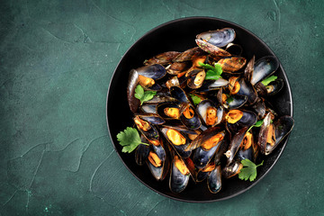Top view of freshly cooked mussels with parsley on dark turquoise background