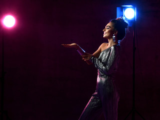 Smiling woman in silver dress singer actress is on stage in neon lights holds hand up with open palm for object paste
