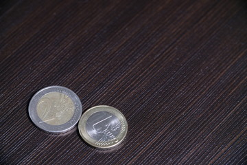 metal coins of one euro and two euros lie on a black table.
