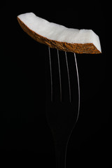 Bright piece of coconut on a fork on a black background close-up.