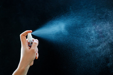 Close up of using antibacterial hand spray on black background.