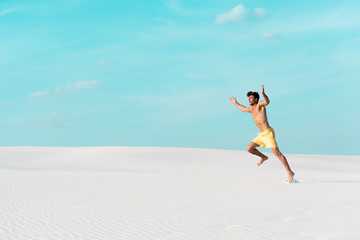 man in swim shorts with muscular torso running on sandy beach