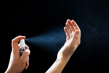 Man hands using sanitizer spray for hand hygiene on black background. - obrazy, fototapety, plakaty