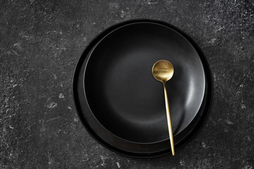 Top view of empty black plate with gold spoon on black background