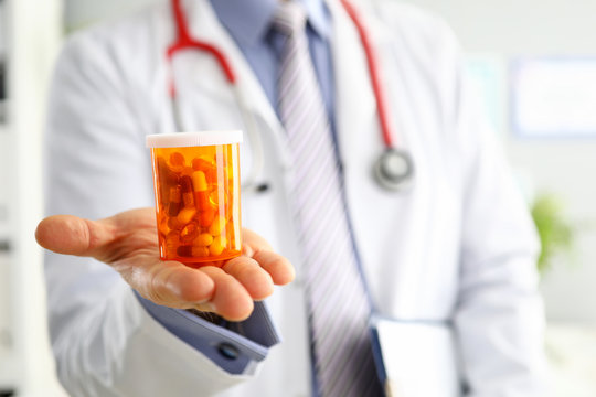 Male Medicine Doctor Hand Holding And Offering To Patient Jar Of Pills
