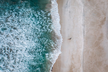 Fototapeta na wymiar View from a drone girl lies on a sandy beach next to the blue waves of the Pacific Ocean in Mexico