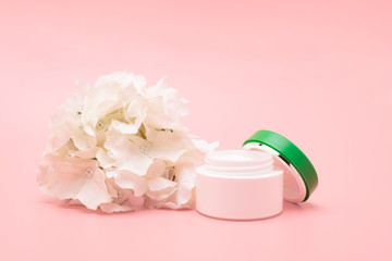Cosmetic cream container and pink flowers on white wooden background from top view