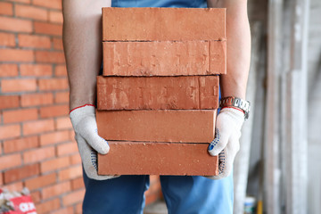 Gloved builder manually carries brick construction