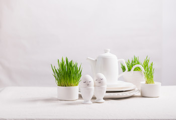 Festive composition Easter eggs in cups and green plant sprouts on a white table. Light background Happy Easter concept.