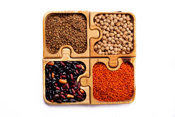 Legumes in brown wooden puzzle form on a white background. Green and red lentils, beans and chickpeas