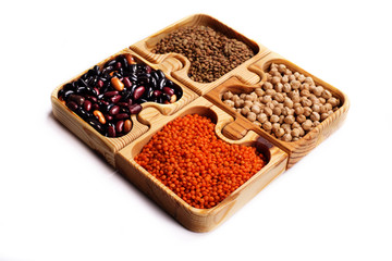 Legumes in brown wooden puzzle form on a white background. Green and red lentils, beans and chickpeas