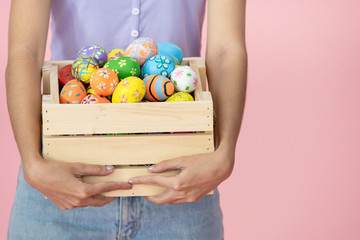 Cheerful Asian pretty girl holding up a wooden basket with colorful Easter eggs inside. Colourful Easter eggs in the festival celebrating. Cute girl's portrait in Easter egg festival concept.