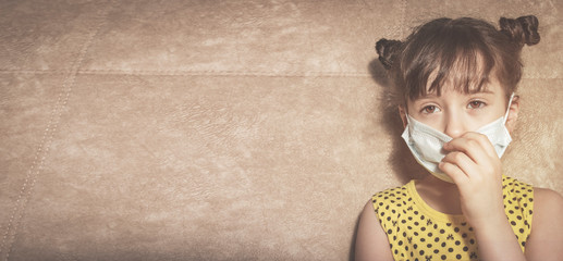 A little girl in a yellow dress wants to remove the protective medical mask. The concept of pandemic protection covid-19. Space for text