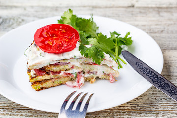 Zucchini cake with tomatoes and fresh parsley on white wooden background.