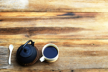 Black coffee with black kettle in white cup on rustic wooden table top view