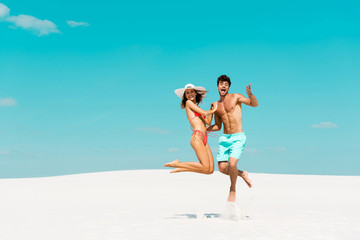 smiling young couple jumping together on sandy beach