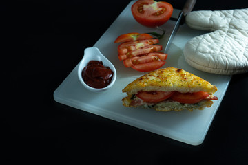 Baked croque monsieur spinach and ham sandwich with tomato sauce, isolated black background.