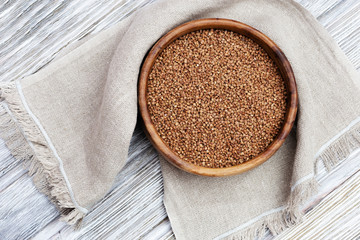 Buckwheats in round rustic bowl on wooden table with sackcloth. Healthy food background with copy space for your text.