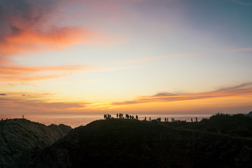 A crowd of people admire the sunset on a cliff on the Pacific Ocean
