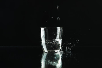 Pouring purified fresh water in glass on mirror background