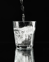 Pouring purified fresh water in glass on mirror background