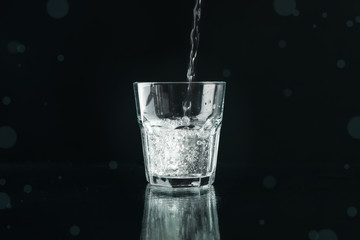 Pouring purified fresh water in glass on mirror background